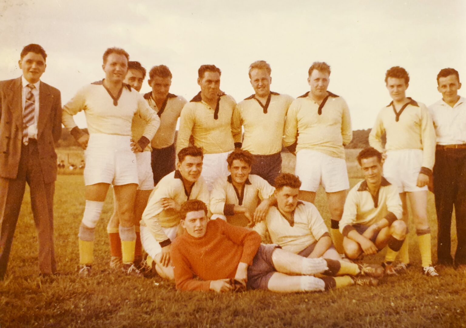 Photographie couleur passée : l'équipe en maillot jaune à col noir et short blanc, huit joueurs debout avec un dirigeant en costume à gauche, quatre accroupis et, allongé devant eux, le gardien en pull orange.
