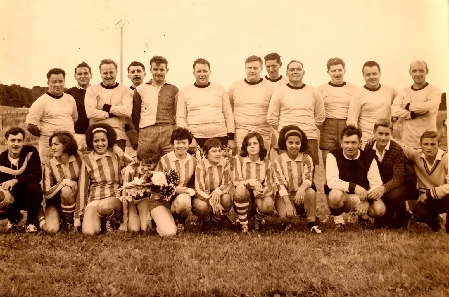 Photographie sépia : les vétérans en maillot clair debout au fond, et devant eux, accroupies, les joueuses de l'équipe adverse en maillot rayé, dont l'une tient un bouquet de fleurs.