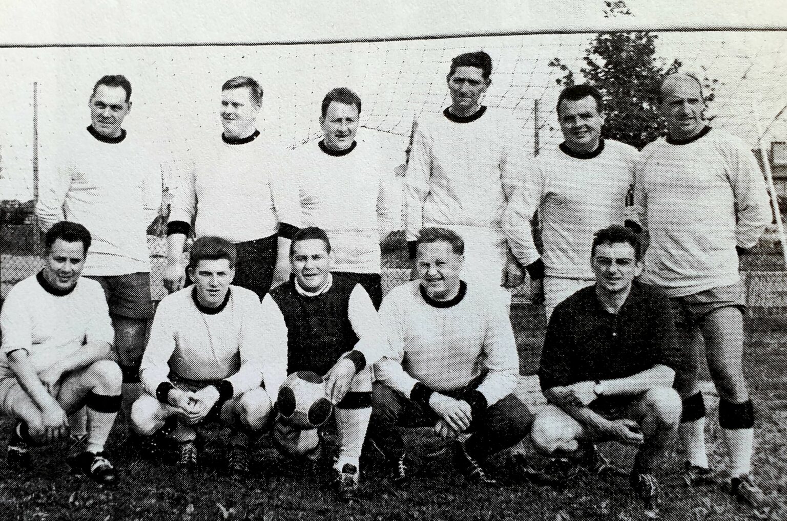 Photographie en noir et blanc de l'équipe devant les buts : six joueurs debout en maillot clair à col foncé, et cinq accroupis devant, dont deux en maillot sombre.