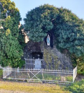 La grotte aujourd'hui : un rocher de pierres sombres envahi de lierre, une statue blanche de la Vierge dans la niche haute sous l'inscription « Immaculée Conception », un crucifix dans la niche basse fermée d'une grille, et une clôture blanche autour.