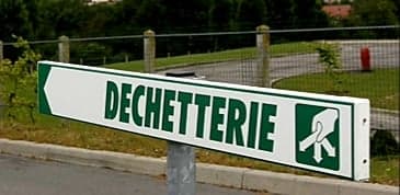 Un panneau routier vert et blanc indiquant « Déchetterie », avec une flèche vers la gauche et un pictogramme de personne jetant un déchet.